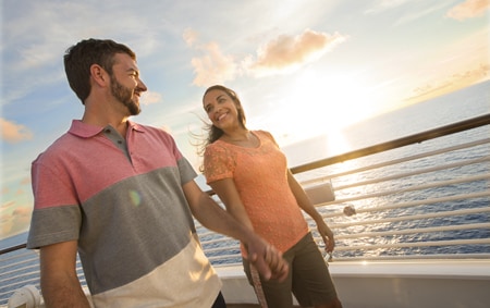 A man and a woman hold hands while strolling along the deck of a Disney Cruise Line ship