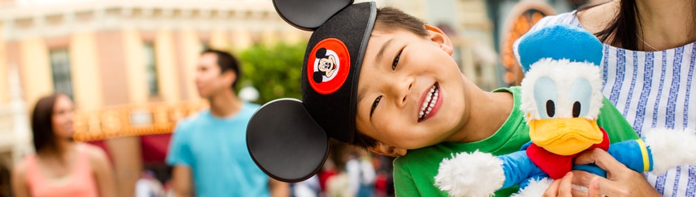 Mother smiles at her son wearing Mickey Ears who is holding a Donald Duck plush toy Mother smiles at her son wearing Mickey Ears who is holding a Donald Duck plush toy