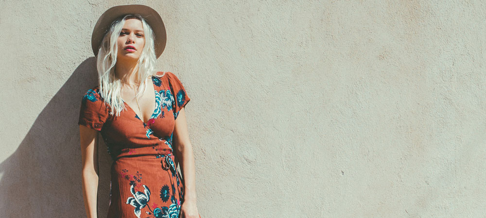 A woman wearing a sundress and sun hat leans against a wall A woman wearing a sundress and sun hat leans against a wall