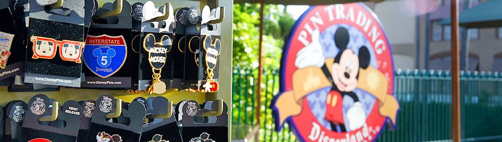 A pin-shaped circular sign outside a shop features Mickey Mouse and reads: Pin Trading Disneyland A pin-shaped circular sign outside a shop features Mickey Mouse and reads: Pin Trading Disneyland
