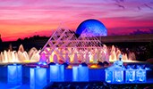 A smiling chef standing behind an illuminated food station at sunset near an active fountain with Spaceship Earth at Epcot in the distance A smiling chef standing behind an illuminated food station at sunset near an active fountain with Spaceship Earth at Epcot in the distance