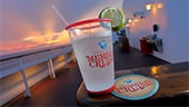 A coaster and chilled drink featuring the Disney Vacation Club MEMBER CRUISE logo on a railing of a ship deck at sunset