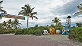 The Mount Rushmore landmark at Disneys Castaway Cay, a banner hanging from palm trees that reads Disneys Castaway Cay, Disney Vacation Club MEMBER CRUISE, Welcome Home and a Disney Cruise Line ship in the distance