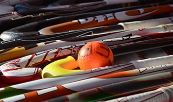 Equipment Drop Off A field hockey ball sits on the ground among several field hockey sticks