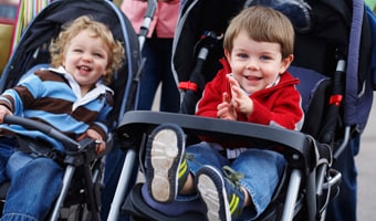 Strollers Two toddlers enjoy a ride in side-by-side strollers