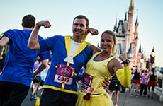 Runners dressed as Belle and Beast pose in front of Cinderella Castle during Disney Princess Half Marathon at Walt Disney World Resort.
