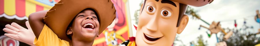 A smiling young boy dressed in a Woody costume T shirt and hat stands beside Woody at Toy Story Land A smiling young boy dressed in a Woody costume T shirt and hat stands beside Woody at Toy Story Land