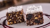 2 cubes comprised of chocolate, seeds and nuts topped with shredded coconut