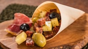 A cornucopia filled with dried meats, blocks of cheese and olives