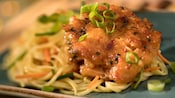 A shrimp cake resting on a bed of noodles, carrots and onions