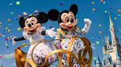 Mickey Mouse and Minnie Mouse standing atop a parade float near Cinderella Castle