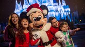 Cuatro miembros de una familia rodean a Mickey vestido de Santa Claus, frente al Cinderella Castle iluminado durante las fiestas