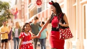 Mother and daughter holding hands and walking together while dressed in Minnie Mouse-themed apparel