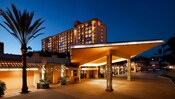 Exterior view of a Good Neighbor Hotel at night featuring a lit sidewalk lined with palm trees