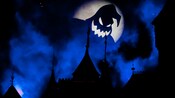 oogie boogie grins in silhouette over sleeping beauty castle which is awash in darkness