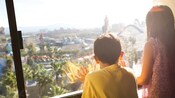 A girl and her younger brother look out a window onto Disney's California Adventure Park