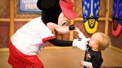 A toddler touches the tip of Mickey's nose; Mickey touches the toddler's nose