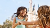 Soap bubbles float near 2 girls who hold hands and twirl, with Cinderella Castle in the background