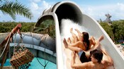 A couple sharing a raft slide backwards down Crush 'n' Gusher water coaster