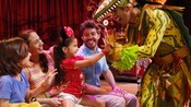 A young girl siting with her family gives a stage performer a double high five during Festival of the Lion King