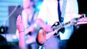 A womanâs hand rising out of the crowd as a guitar plays on stage at an Eat to the Beat performance.
