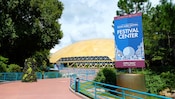 A sign outside a domed pavilion reads Celebrating 20 Years, Epcot International Food and Wine Festival, Festival Center, Open Daily, 9 A.M. to Park Close