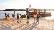 Pequeños piratas marchan en una playa mientras un miembro del elenco saluda con la mano