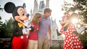 A middle-aged couple in front of Cinderella’s Castle chat with Mickey Mouse and Minnie Mouse