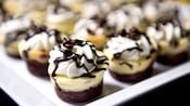 Chocolate sauce drizzled atop a whipped-cream garnish on dozens of bite-sized chocolate cheesecakes