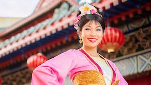 Mulan smiles by the China Pavilion at Epcot wearing a colorful Chinese robe and flowers in her hair