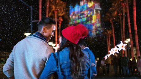 a couple looks at palm trees and a building covered in festive lights - Hollywood Studios Christmas Lights a couple looks at palm trees and a building covered in festive lights - Hollywood Studios Christmas Lights