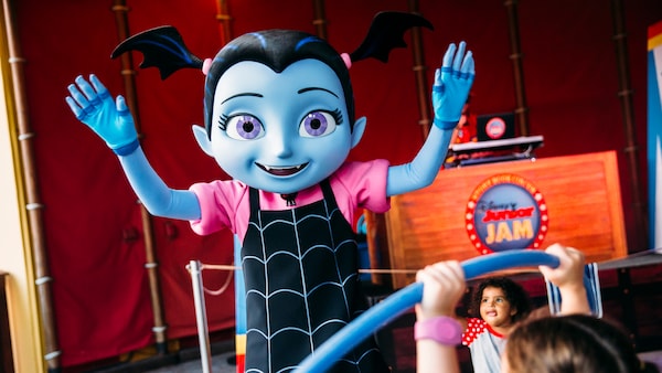 Vampirina stands with her arms raised near a sign that reads 'Disney Junior Jam'