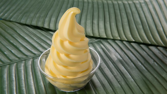 A pineapple soft serve dessert in a clear bowl on banana leaves