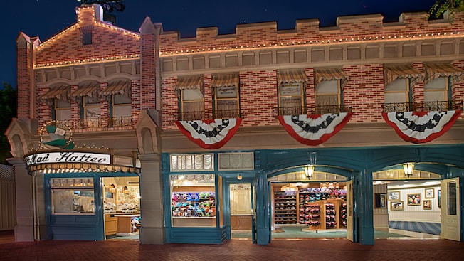Patriotic flags cascading from the storefront as lights outside The Mad Hatter illuminate the night