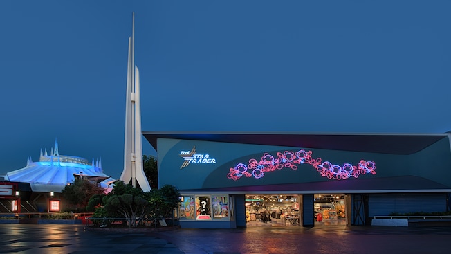 The exterior of Star Trader lights up in evening as spires atop Space Mountain extend toward the sky