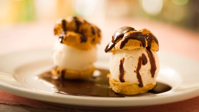 Two puff choux pastries filled with vanilla ice cream and sprinkled with chocolate sauce on a plate