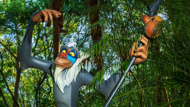 Rafiki the baboon holds his staff in front of jungle trees