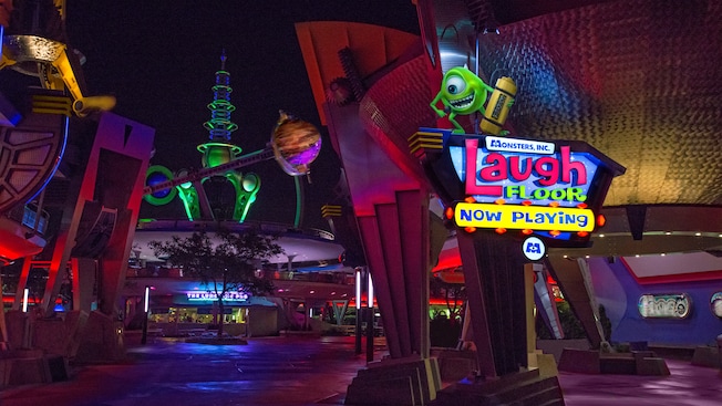 A statue of Mike Wazowski stands atop a sign for Monsters, Inc. Laugh Floor in Tomorrowland at night