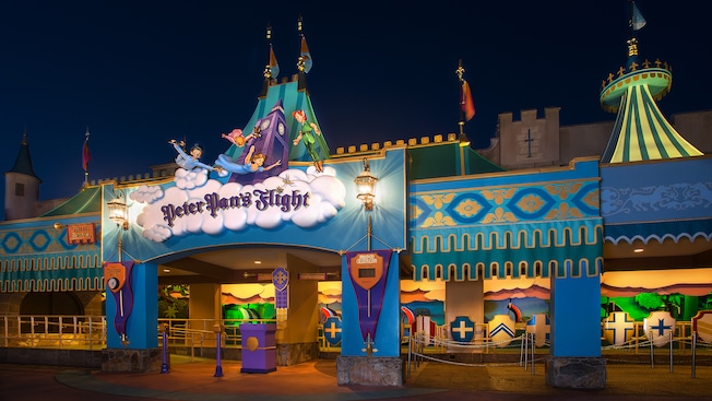 Night view of Peter Pan's Flight with statues of Peter Pan, Wendy and her brothers above its sign