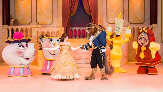 The Beast dances with Belle on stage while Lumiere, Cogsworth, Mrs. Potts and Chip look on in glee