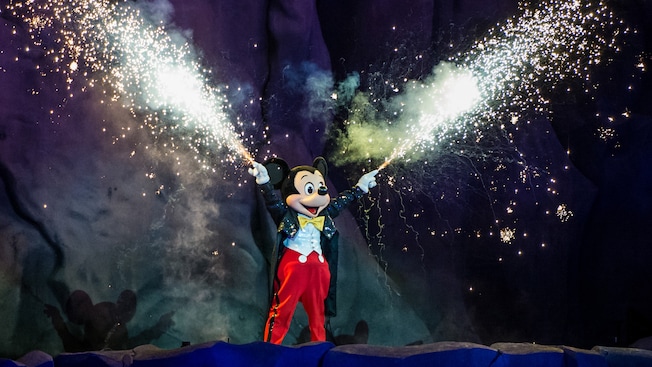 Mickey extends his arms and smiles while thousands of fiery sparkles fly forth from his fingertips