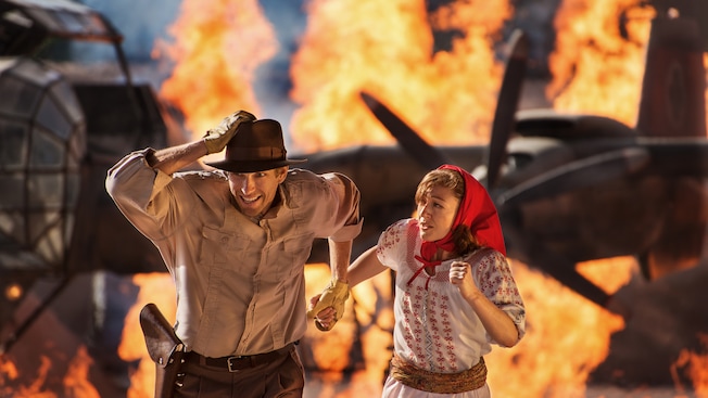 Indiana Jones and Marion run on a fiery set of the Indiana Jones Epic Stunt Spectacular