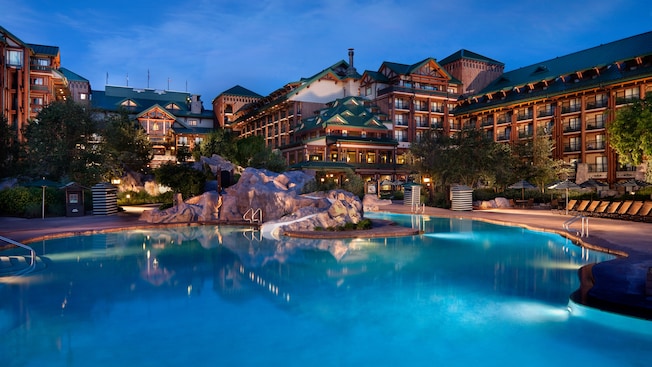 A pool area with artificial boulders, lounge chairs, parasols and a waterslide inside Disney's Wilderness Lodge