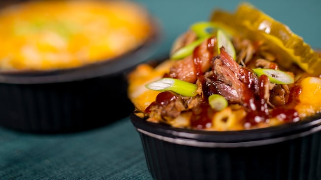 2 ramekins of mac and cheese with one of them topped with pulled pork, pickles and green onions