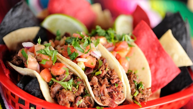 Tacos de barbacoa in corn tortillas topped with diced tomatoes and onions, and garnished with cilantro