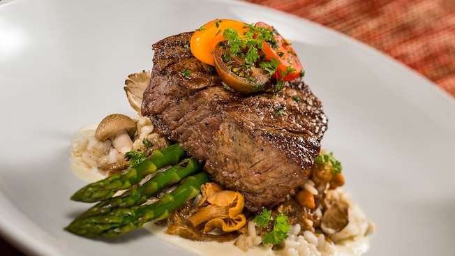 Filet mignon sitting on a bed of asparagus and a mushroom risotto with a white truffle butter sauce