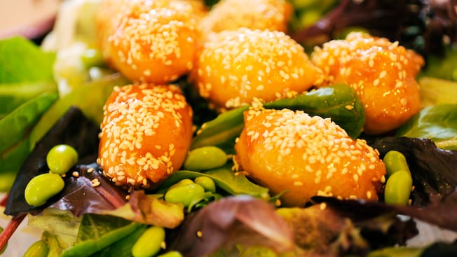 Sesame chicken salad featuring orange chicken served atop a bed of leafy greens and edamame beans