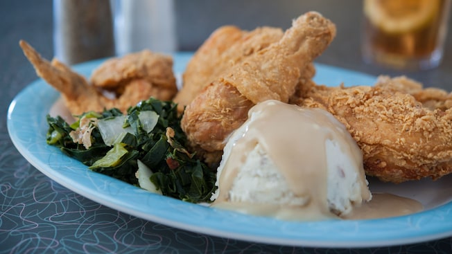 A plate of fried chicken with collard greens, mashed potatoes and gravy