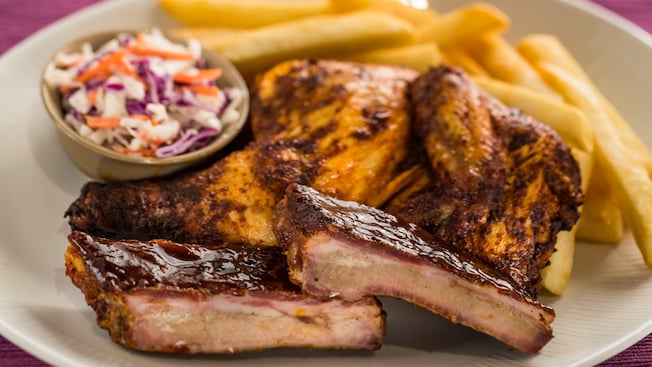 A plate with barbecue pork ribs and a quarter roasted chicken served with cole slaw and french fries
