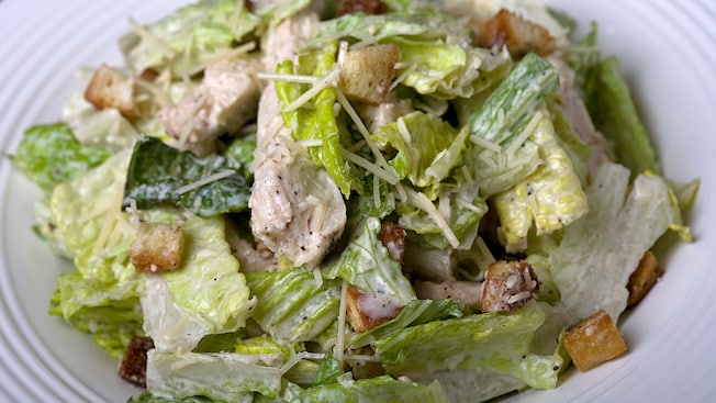 A serving of chicken Caesar salad topped with fresh parmesan cheese, croutons and black pepper